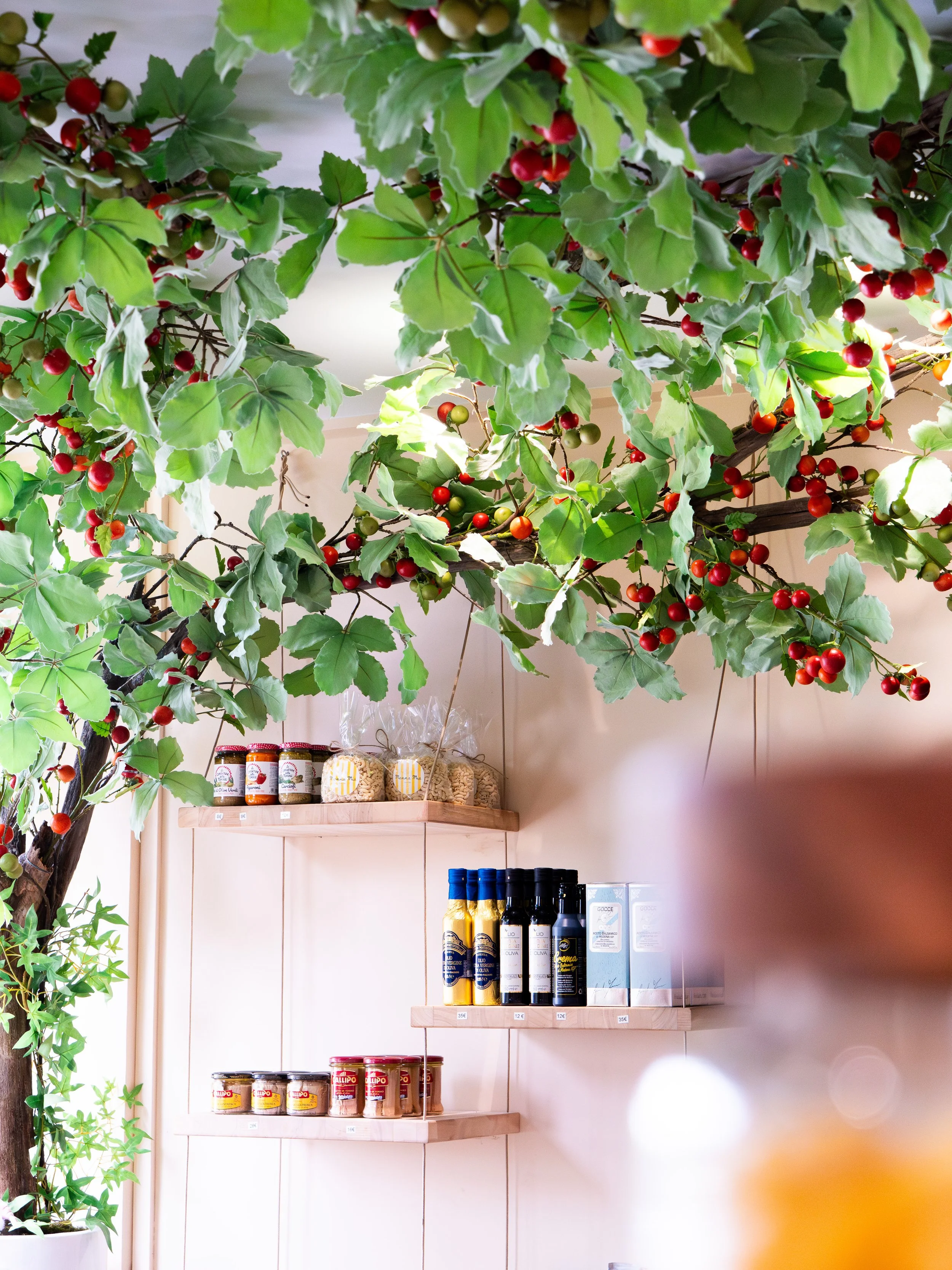 Une étagère en bois avec des bouteilles de condiments et des bocaux de produits alimentaires, entourée de feuilles vertes de plantes en intérieur.