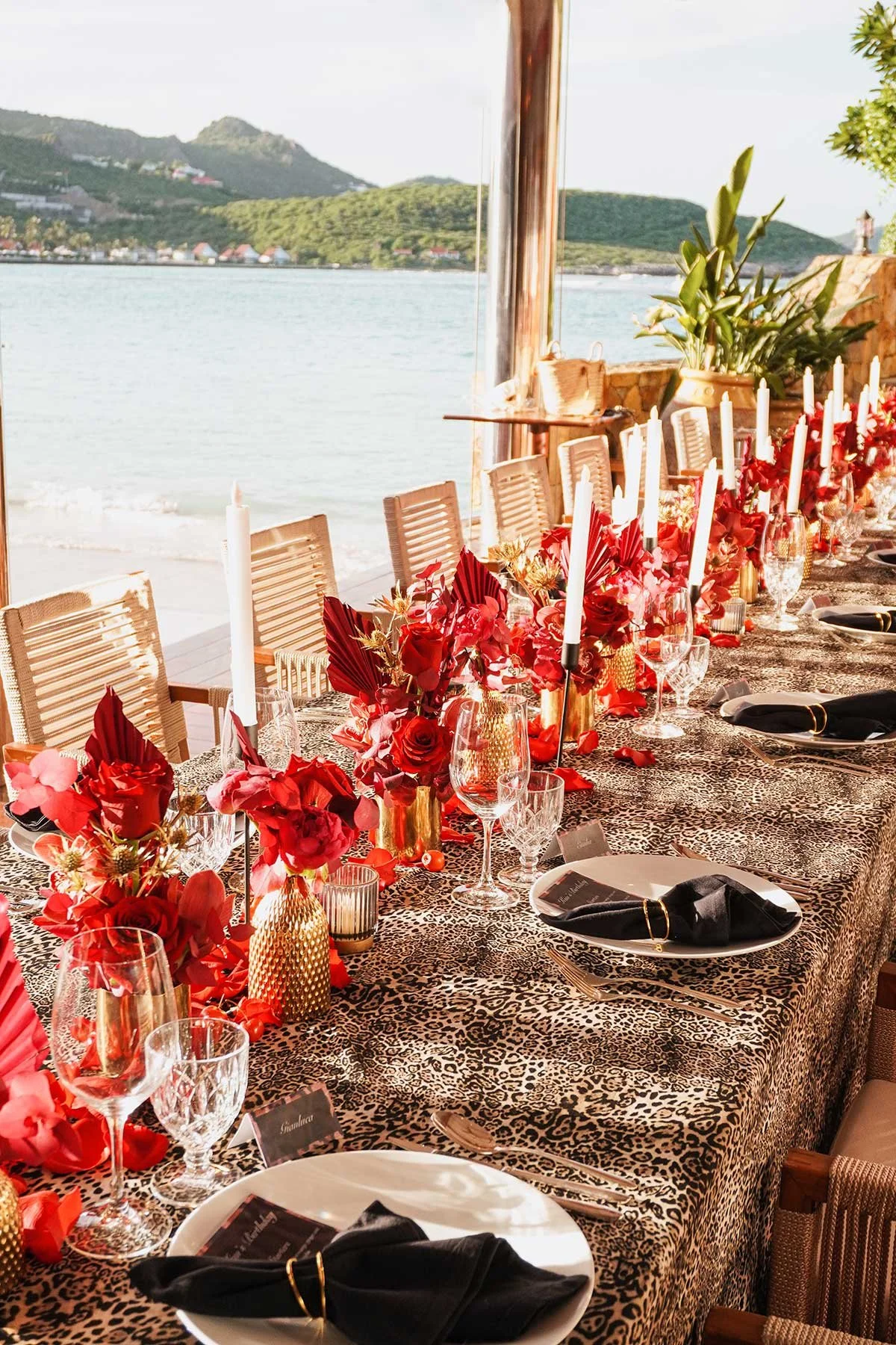 Chic outdoor wedding table with red floral arrangements, black tableware, and ocean view in St Barth.