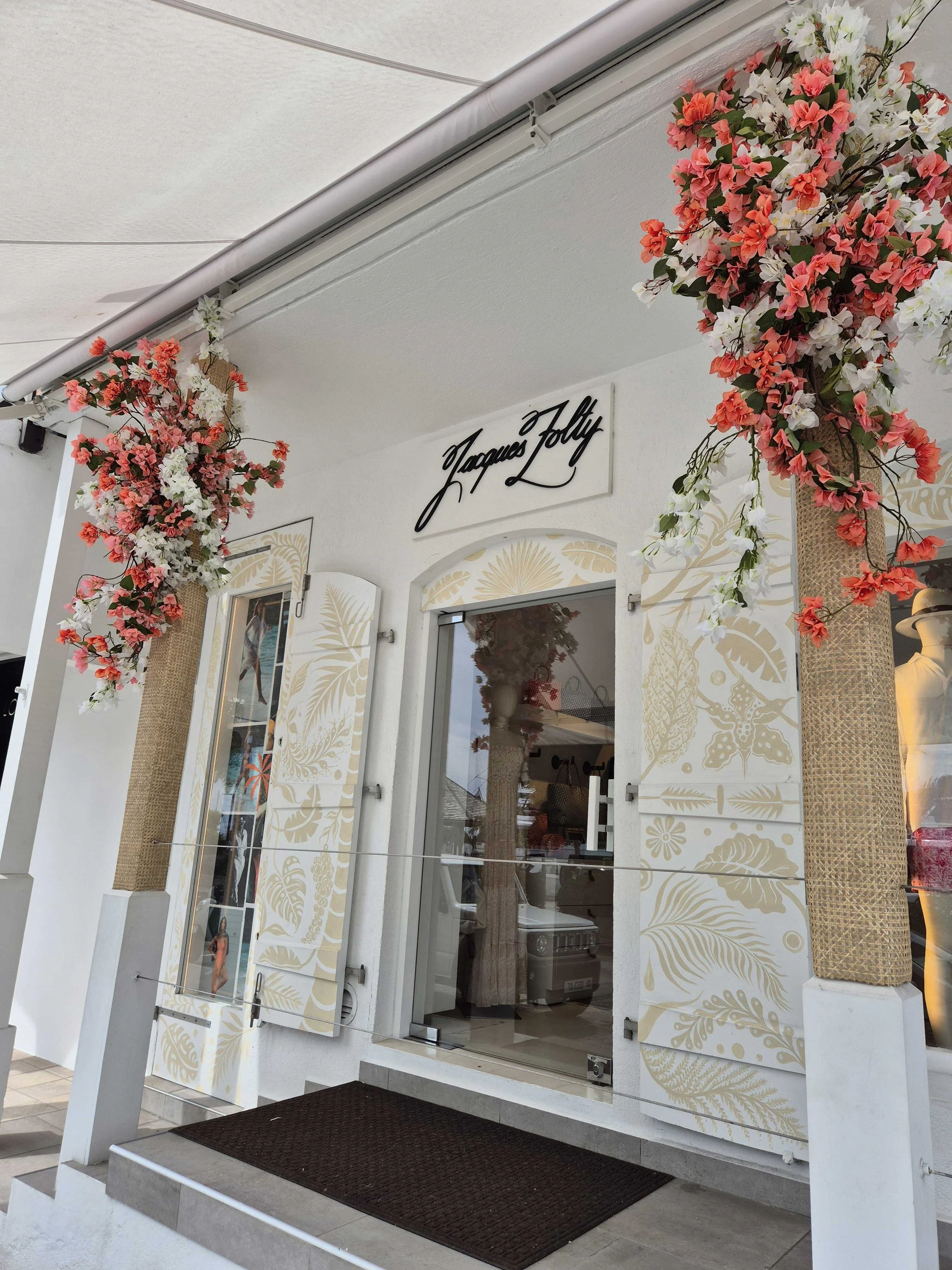 Chic boutique entrance decorated with red flowers and elegant white walls creating a refined tropical atmosphere in St Barth.