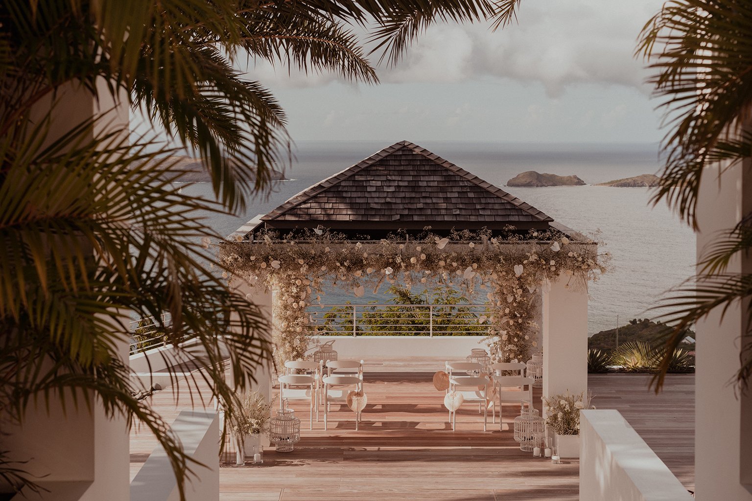 Tropical outdoor wedding ceremony with a floral arch overlooking the sea and nearby islands, framed by palm trees in St Barth.