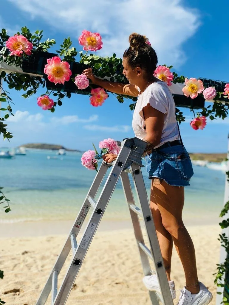 Anaïs, assistant and project manager, creating a floral arch with pink flowers on the beach for a wedding in St Barth.