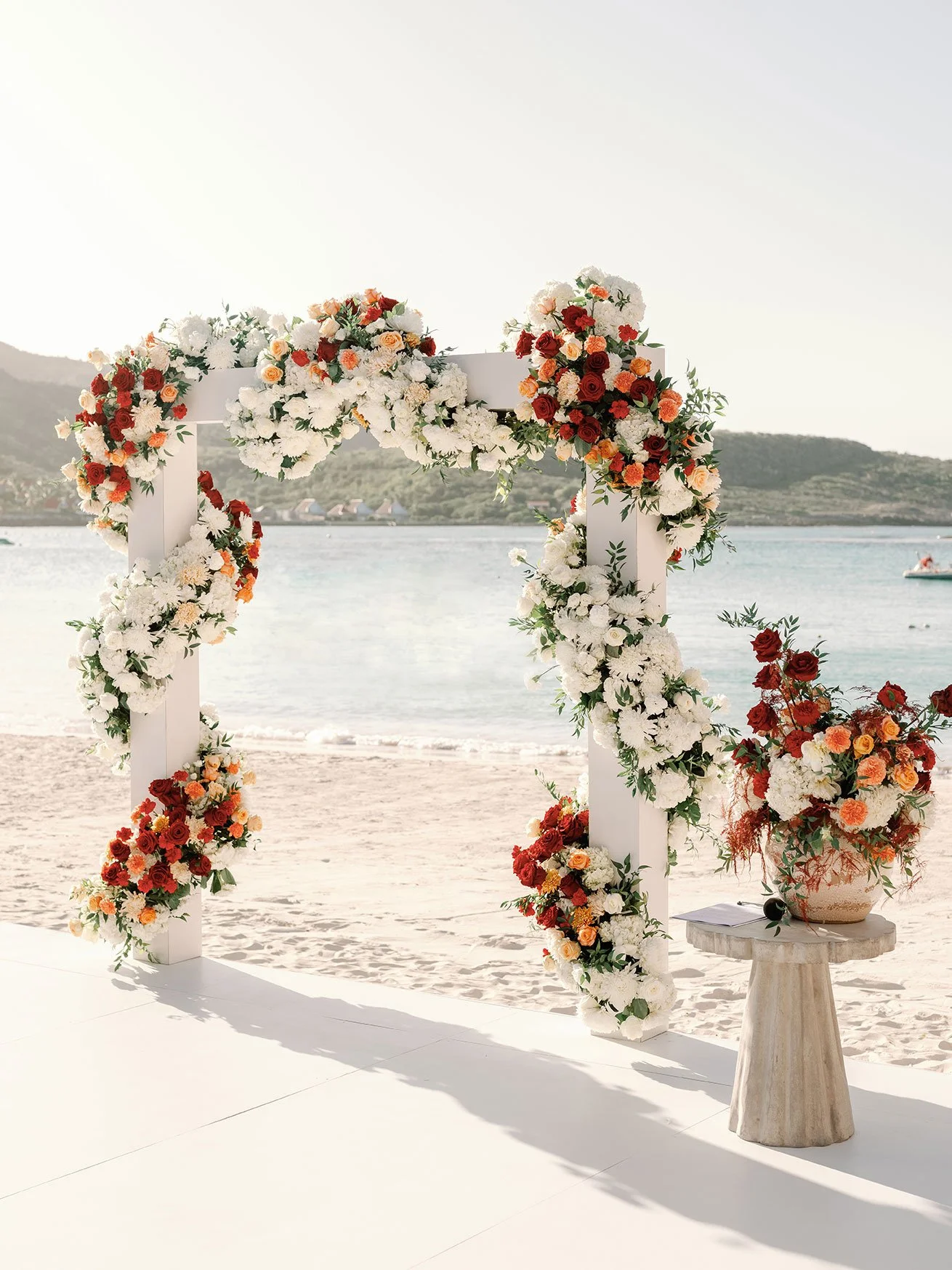 Elegant beach wedding arch with white and orange tropical flowers for a romantic ceremony in St Barth.