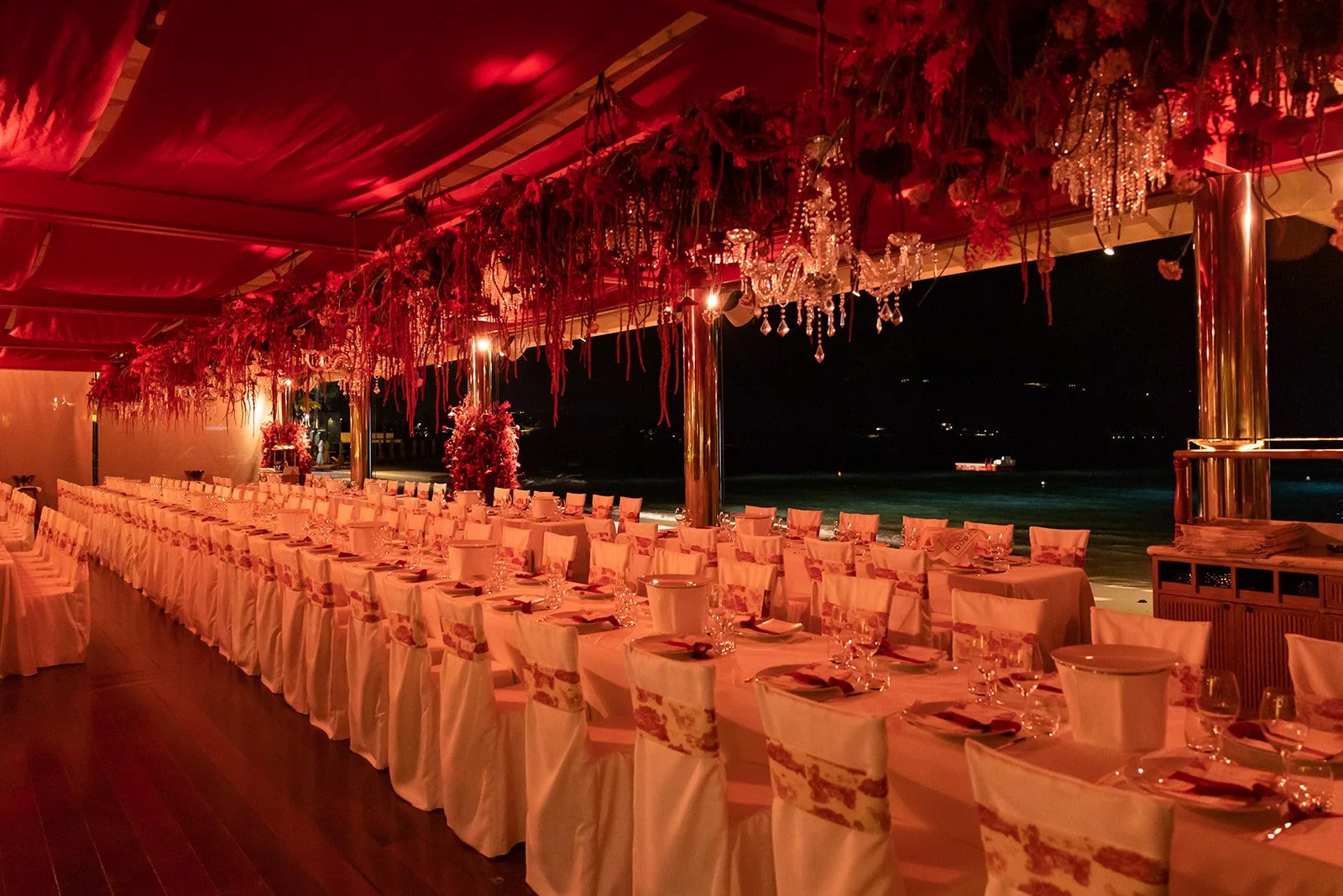 Outdoor wedding dinner setup with long white tables, floral arrangements, and ambient lighting by the sea in St Barth.