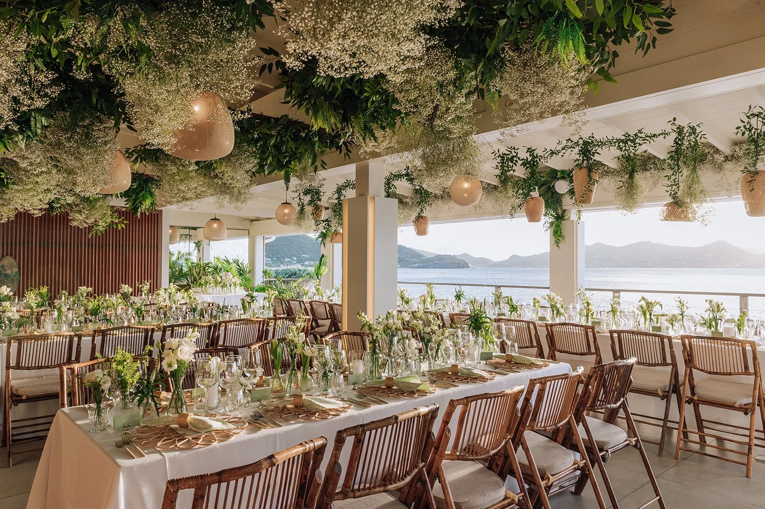 Luxury tropical wedding reception with lush greenery ceiling decor and natural lighting in St Barth.