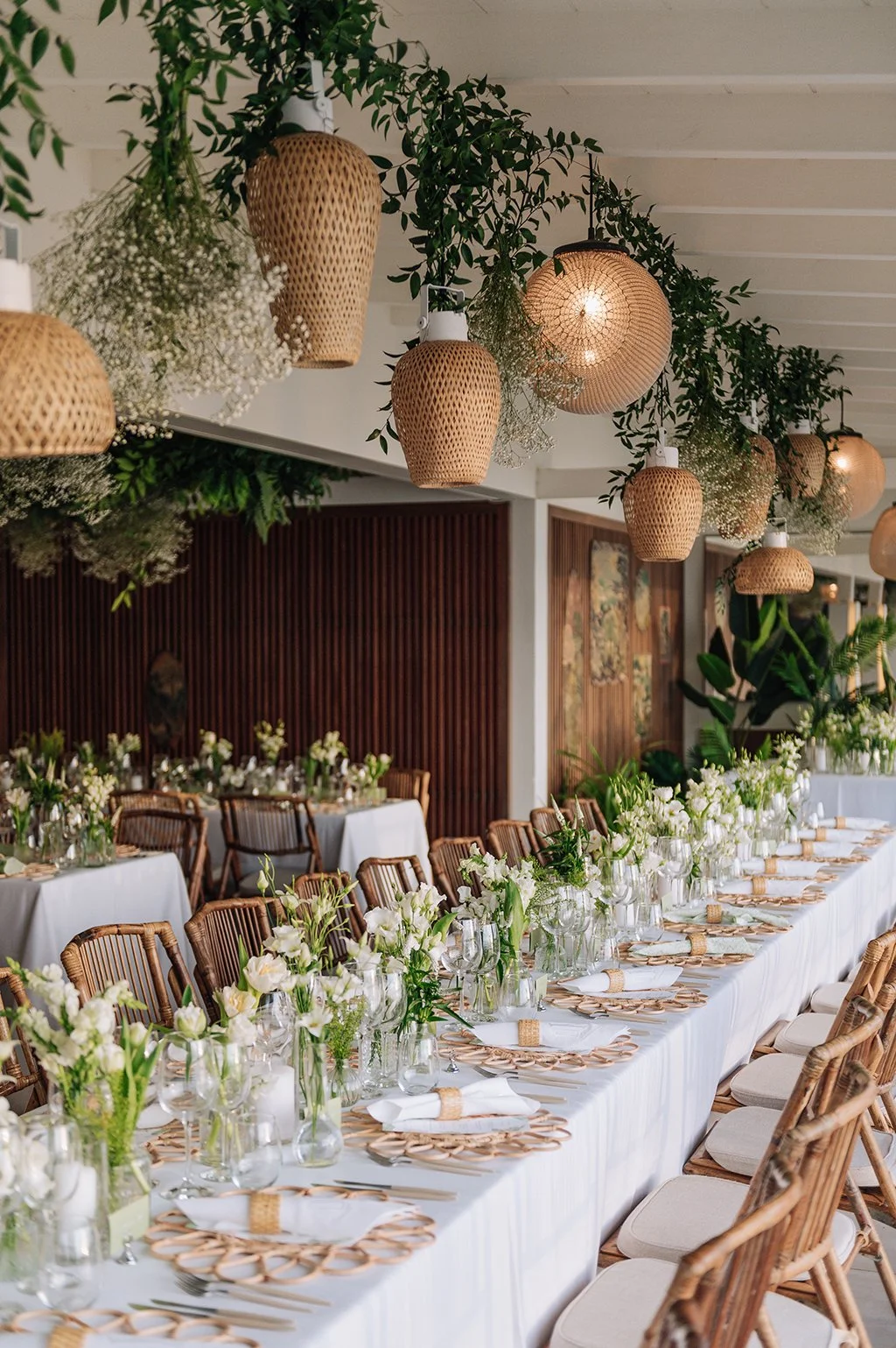 Elegant outdoor wedding dinner setup with hanging lanterns, greenery garlands, and tropical floral decor in St Barth.