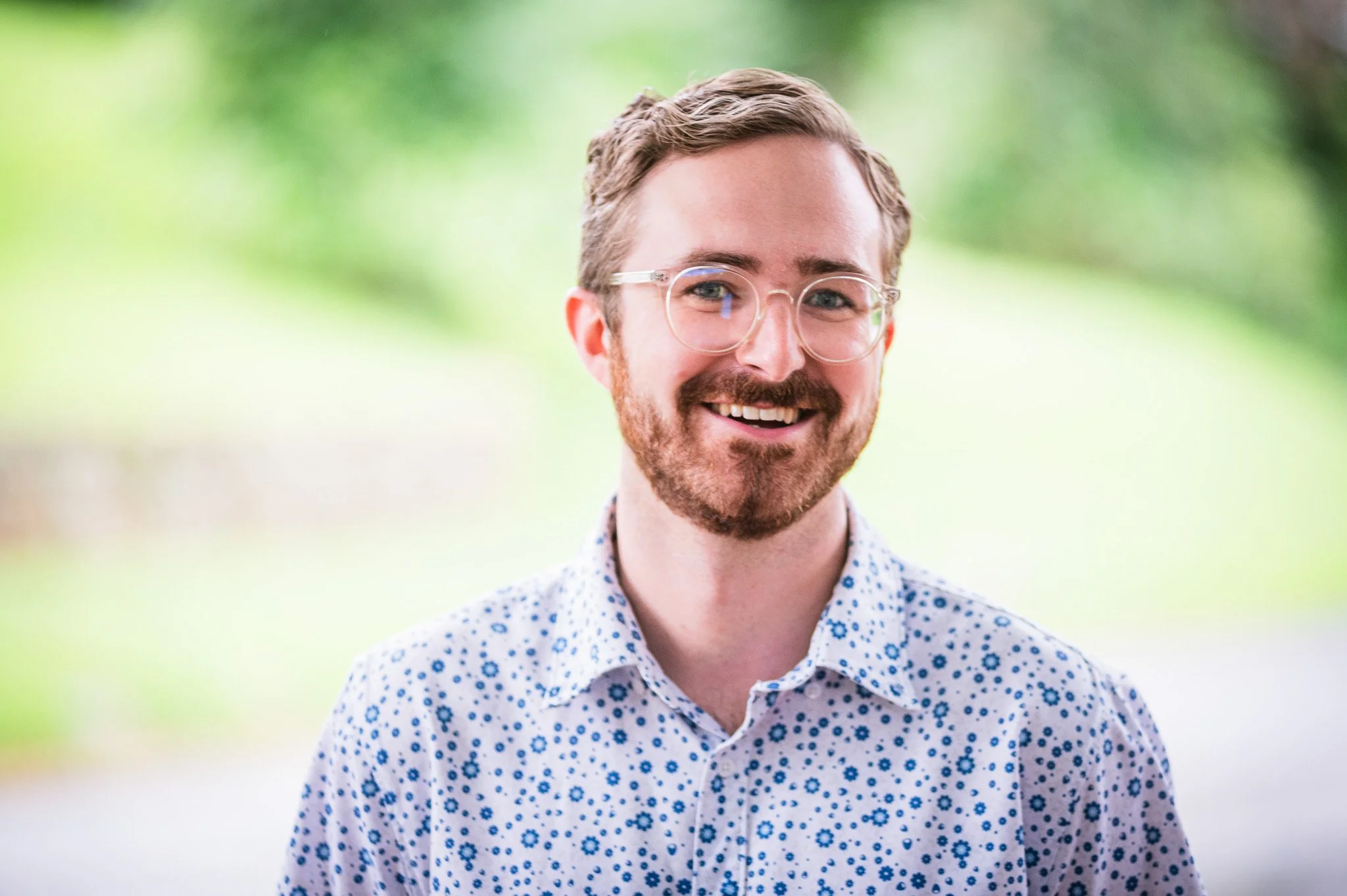 a young man with acetate glasses and a beard smiling at the camera