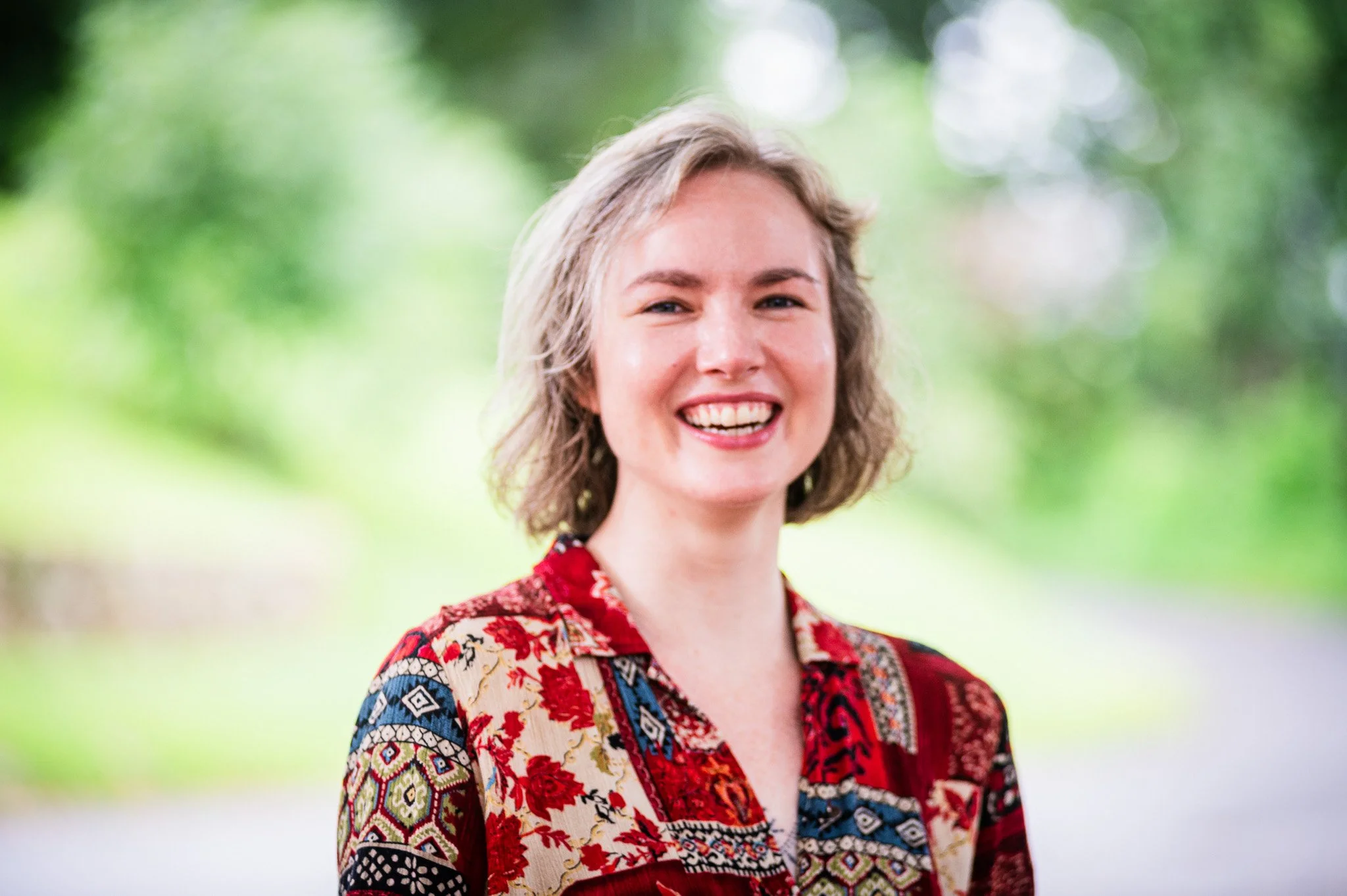 a young person with a colorful quilt-like button down and chin-length hair smiling for a portrait