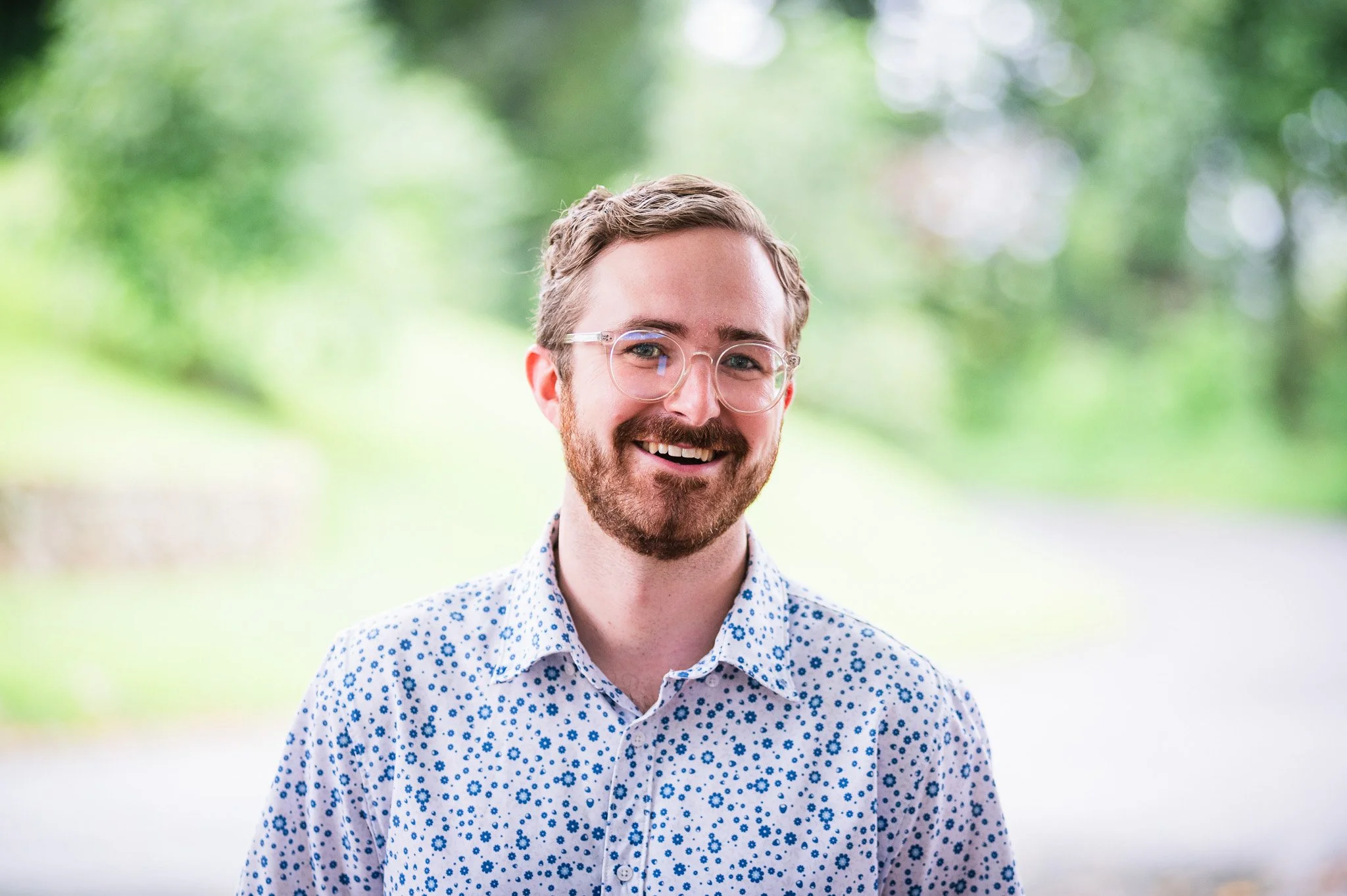 Smiling man with clear glasses and a button up shirt smiling for a teacher portrait