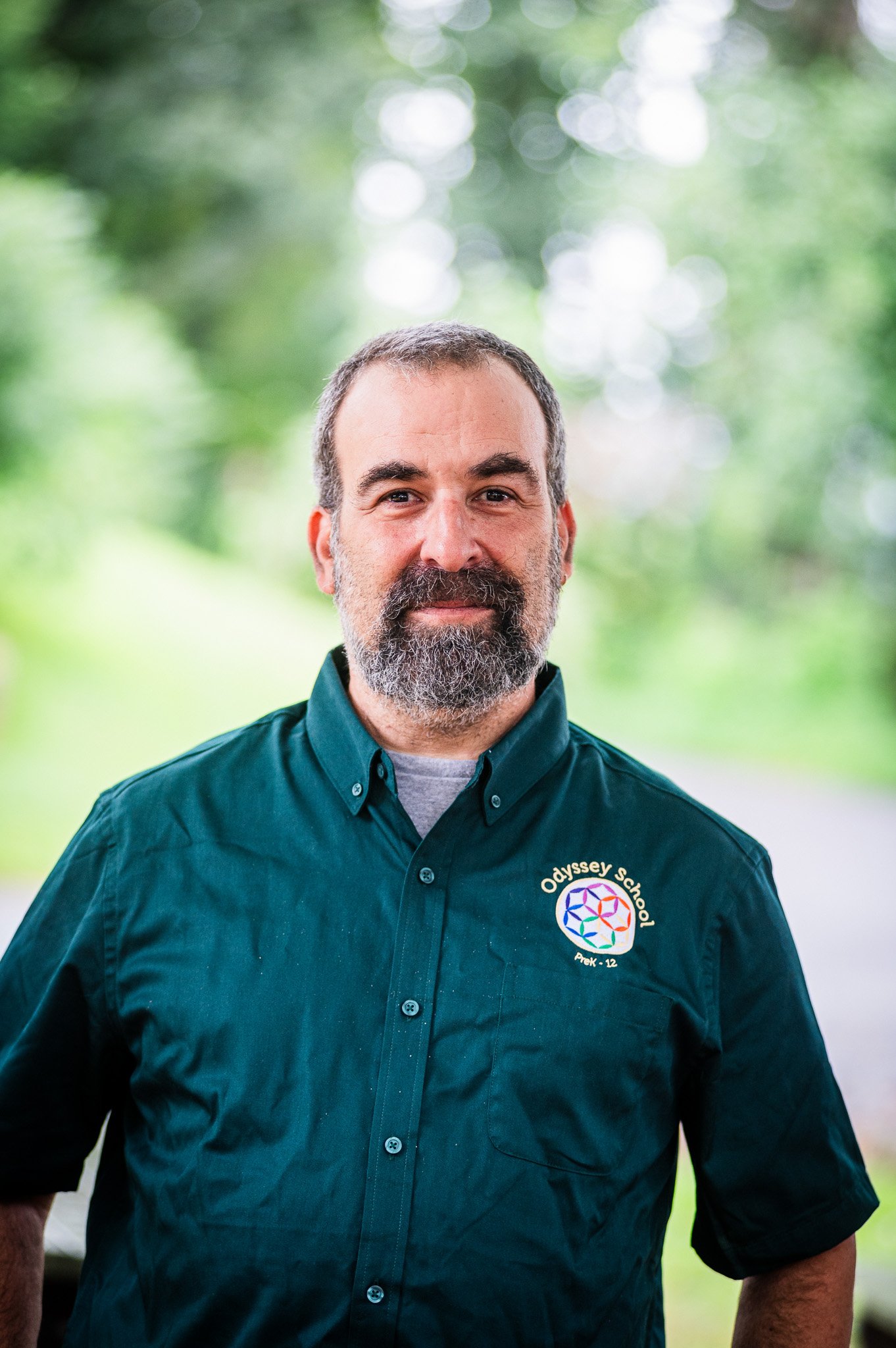 A man with a beard and good eyebrows thoughtfully grinning in an emerald green button down