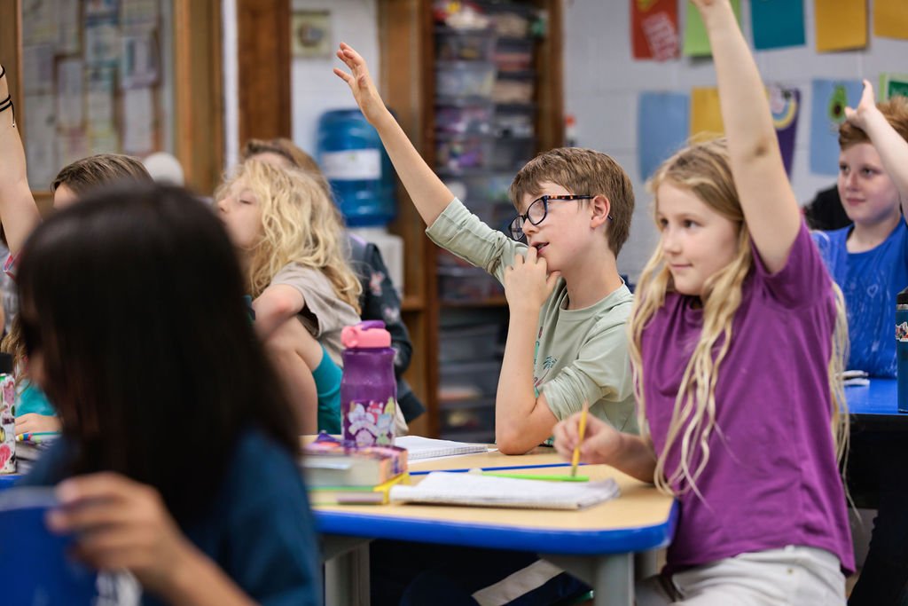 children at an independent school with hands raised in the air to be called on