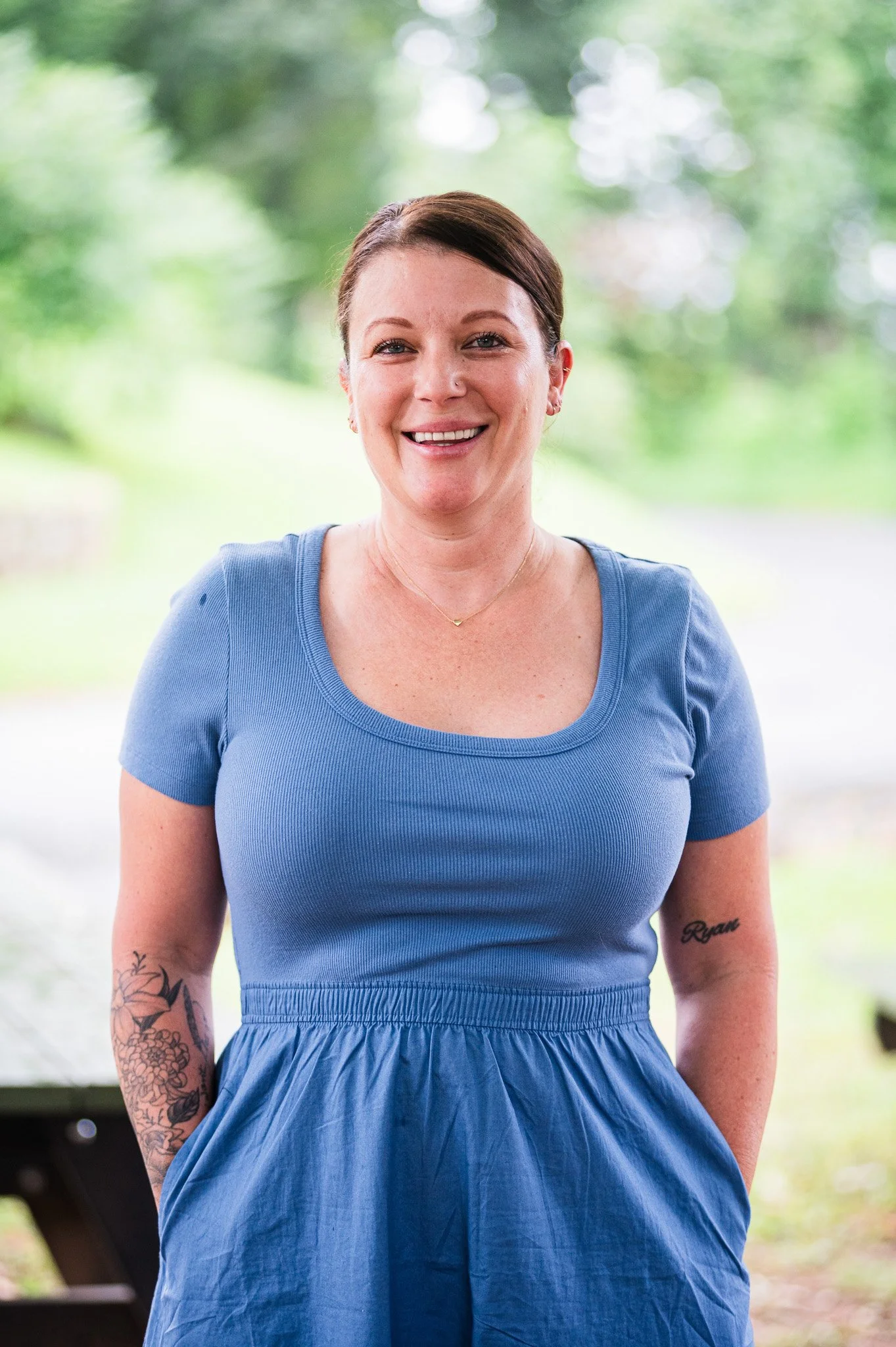 A woman with arm tattoos and pulled-back ponytail smiling on a green background