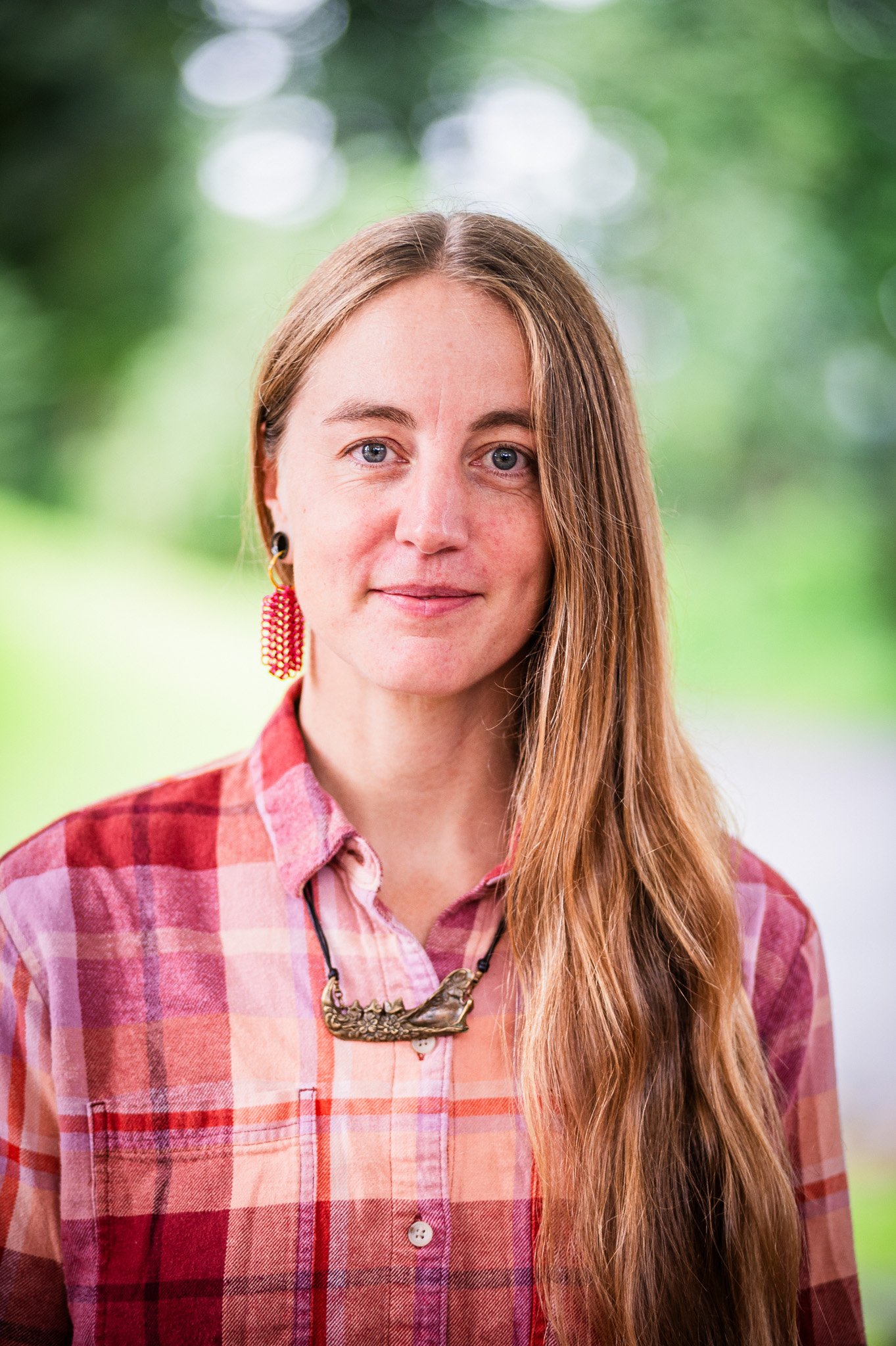a person with long hair and a red plaid button down looking thoughtfully at the camera