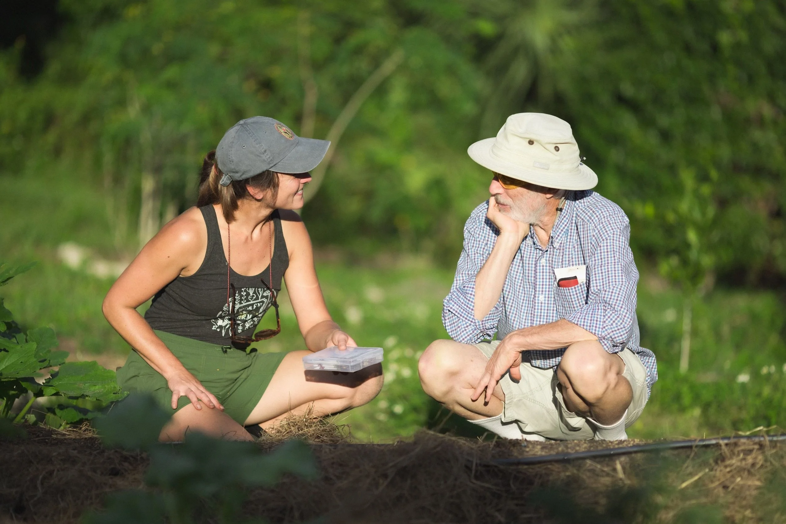 2 people crouching in a garden look at each other