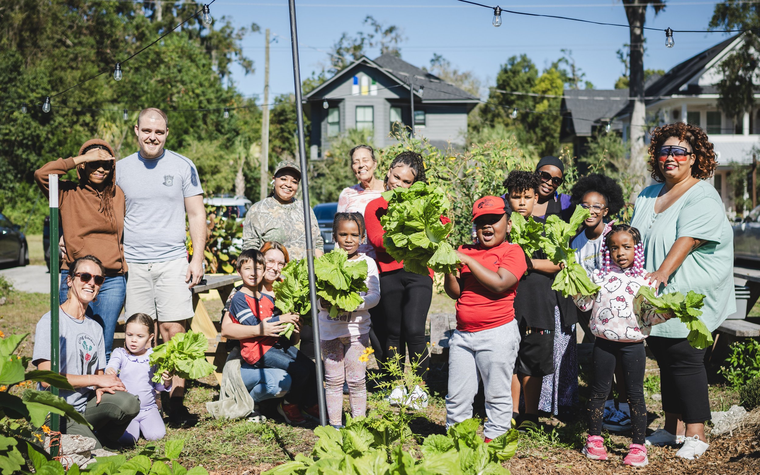 group of people stand in an outside garden holding vegetables