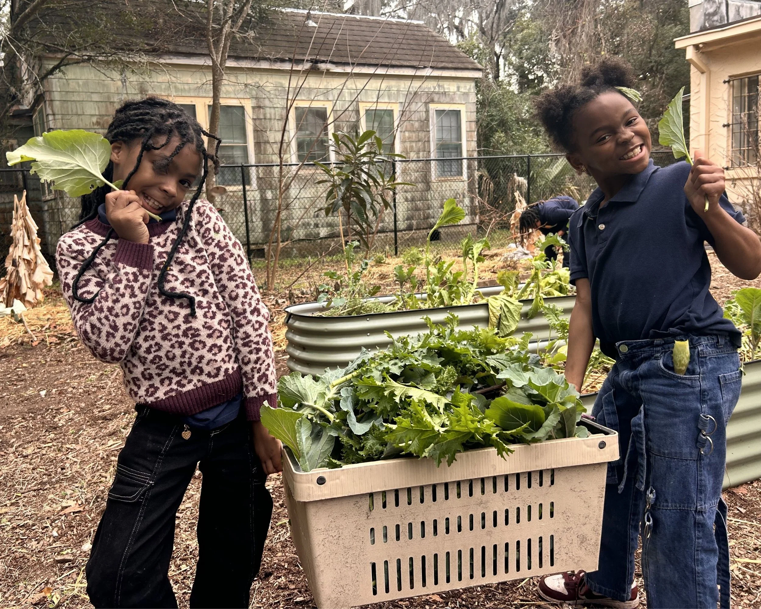 2 children holding a basket of green vegetables they harvested