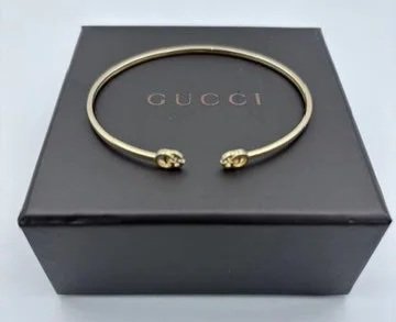 Bracciale Gucci dorato con teste di leone, su scatola nera.