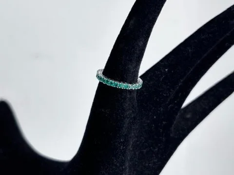 Anello eternity in oro bianco 18K con pietre verdi su espositore nero