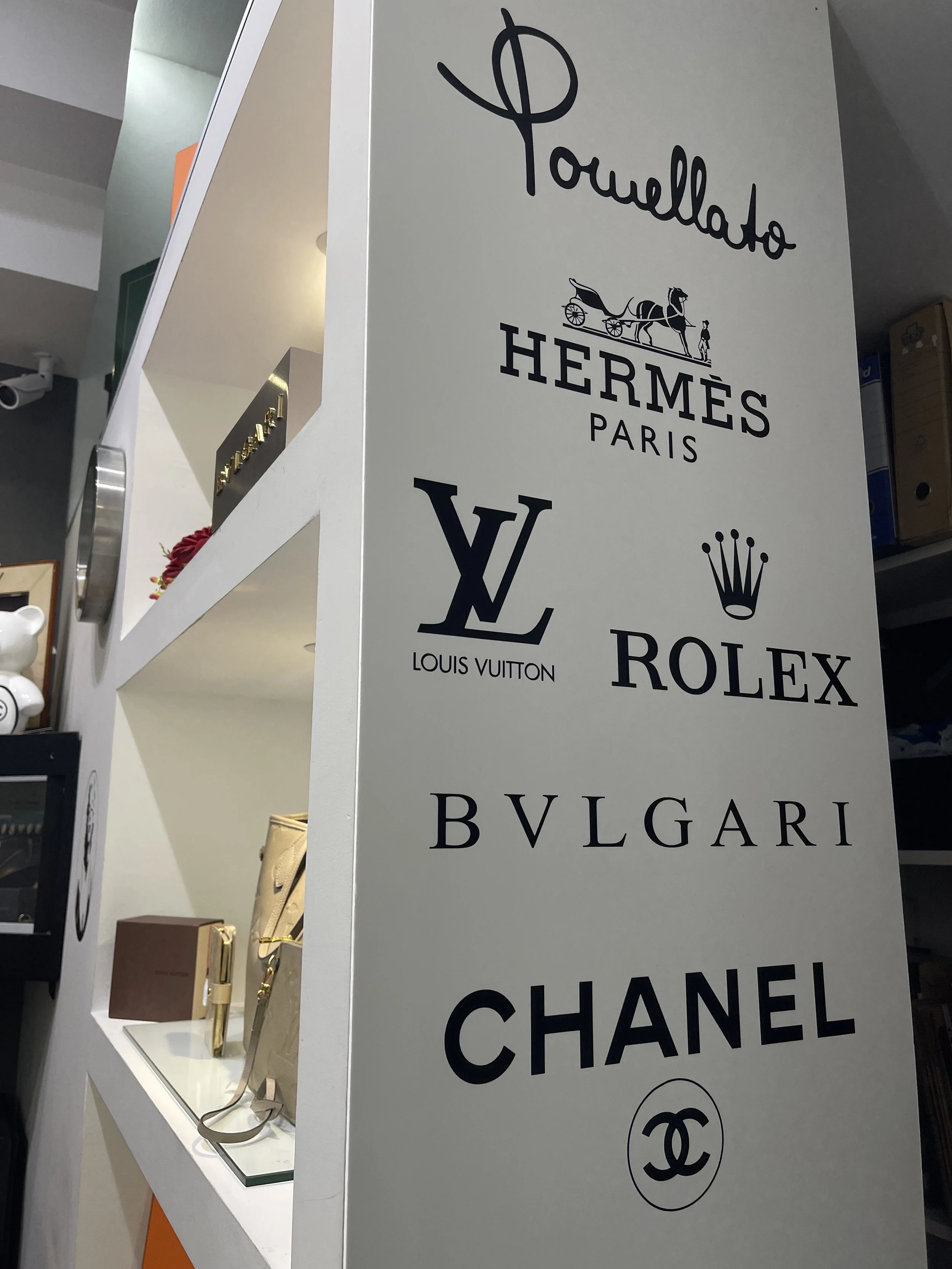Interno della boutique con pannello dei marchi Pomellato, Hermès, Louis Vuitton, Rolex, Bulgari e Chanel