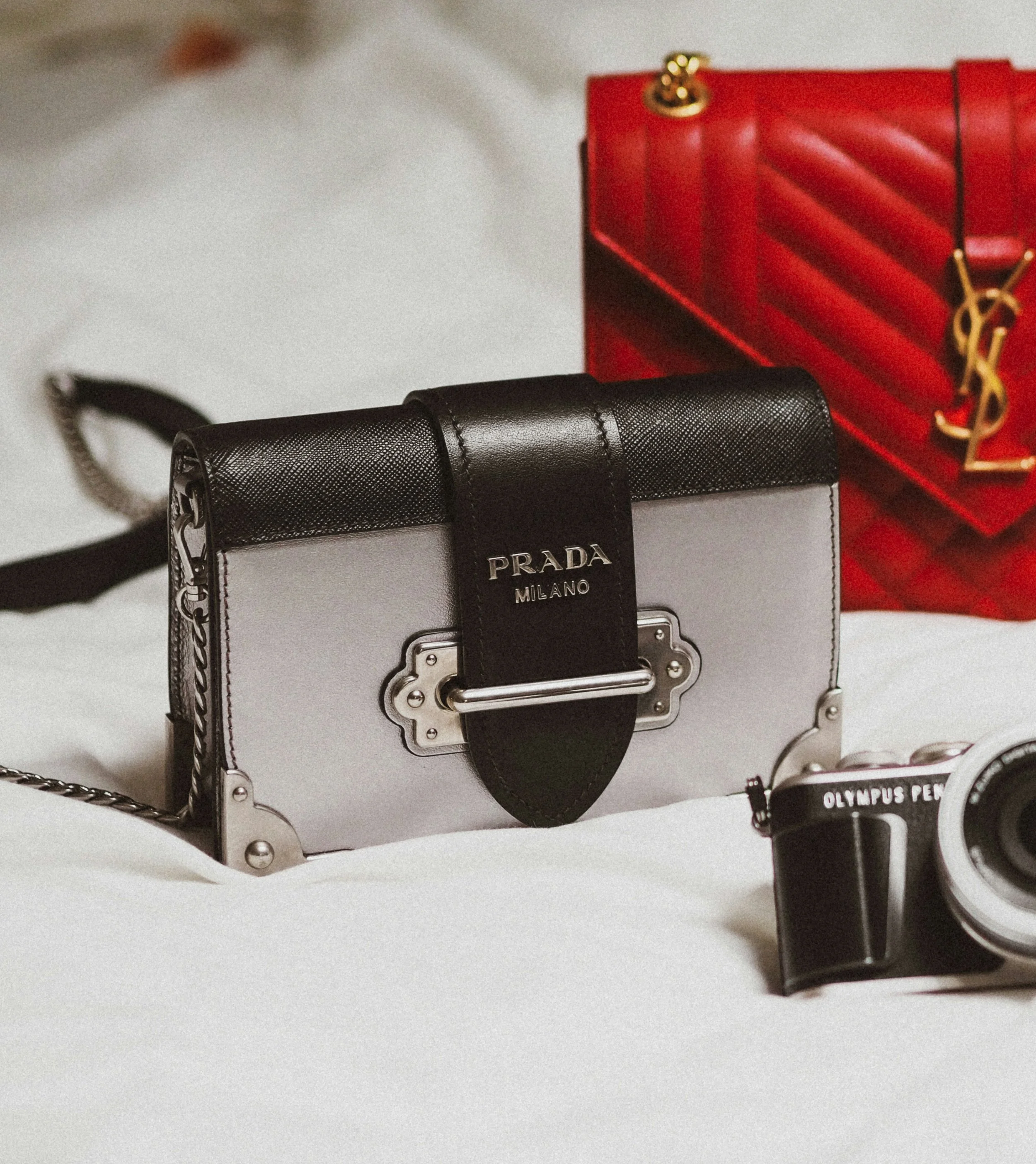 Borsa Prada nera e argento e borsa Yves Saint Laurent rossa con una fotocamera