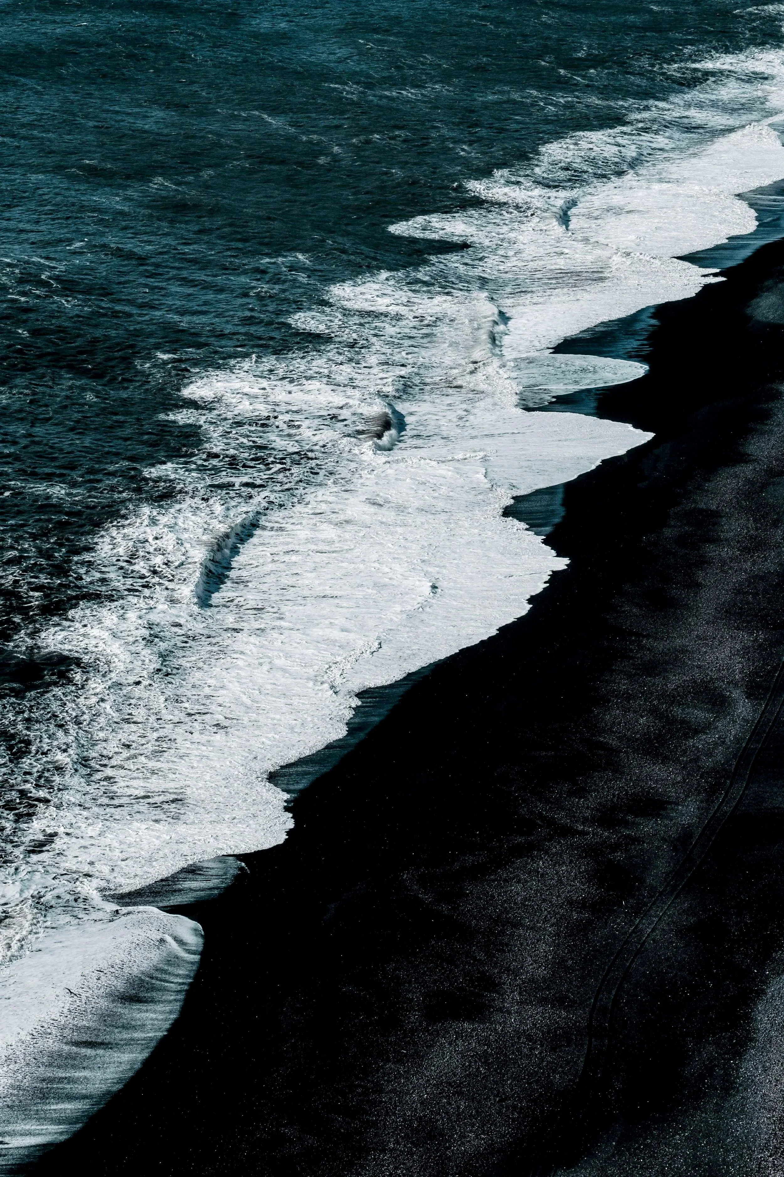Dark rocky shoreline with crashing white waves in the ocean.