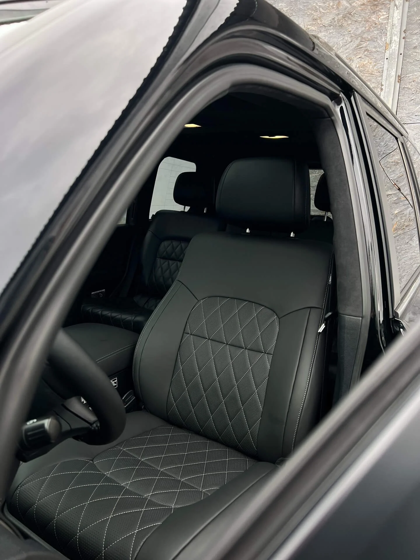 Вигляд через відчинені двері: чорне шкіряне сидіння з білою ромбовидною прострочкою в інтер'єрі позашляховика