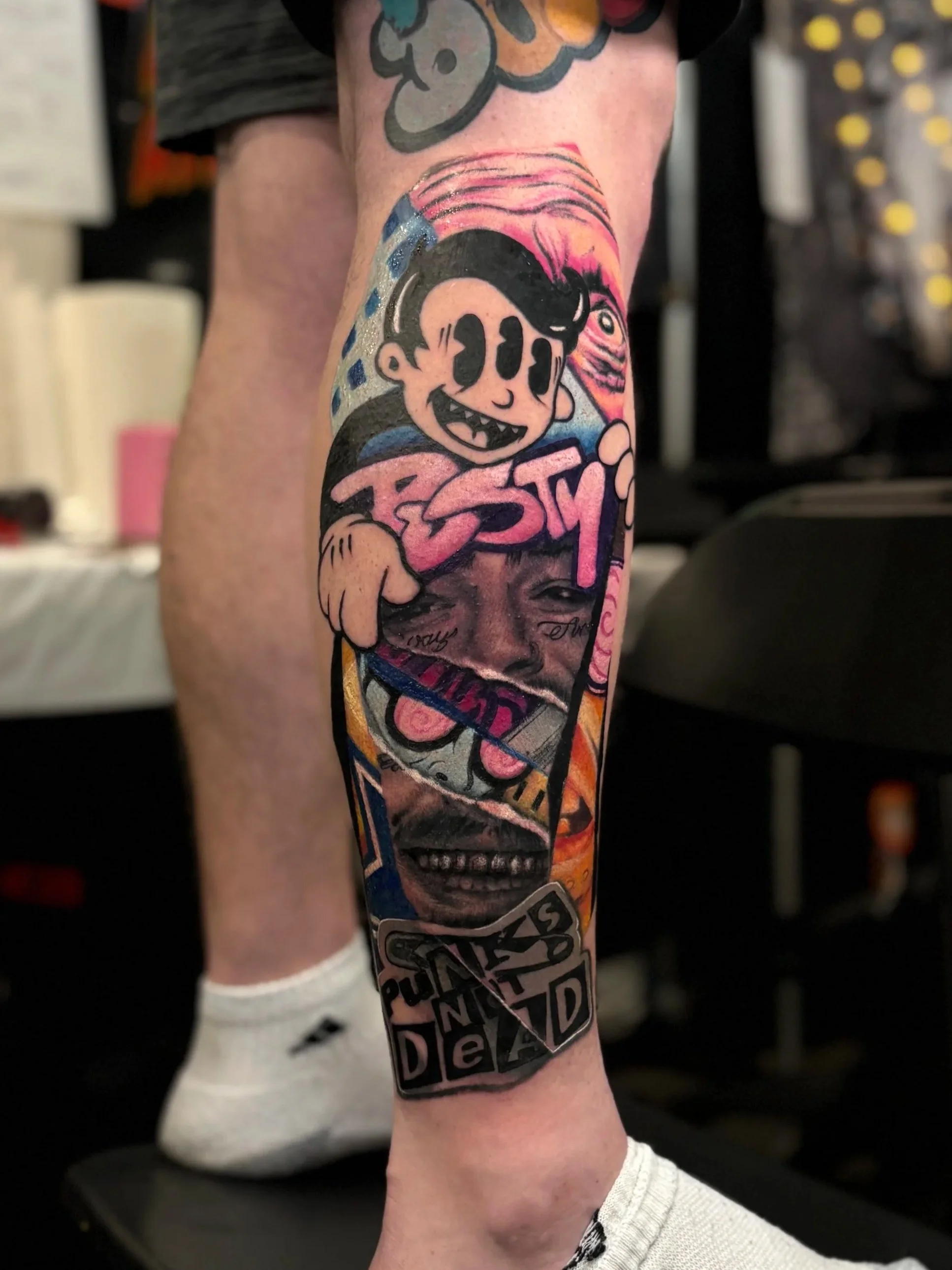 Color collage leg tattoo combining cartoon, portrait and skull imagery by Slush Tattoos