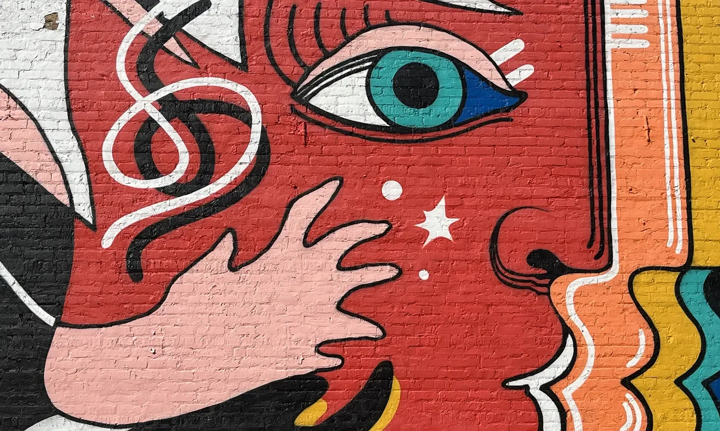 Colorful mural of a face with a large eye, wavy hair, and abstract elements on a brick wall.