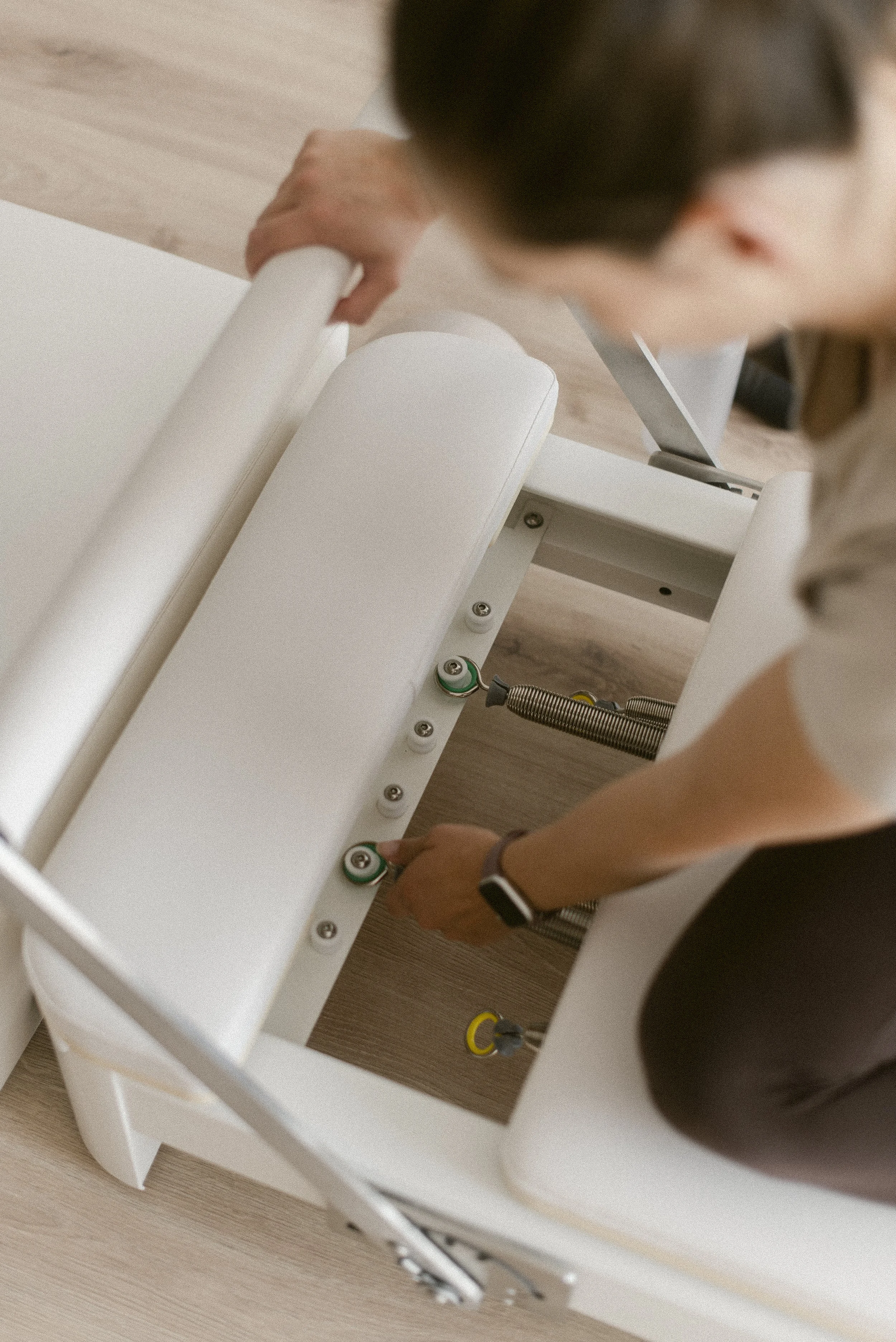 Person adjusting the springs on a pilates reformer machine.