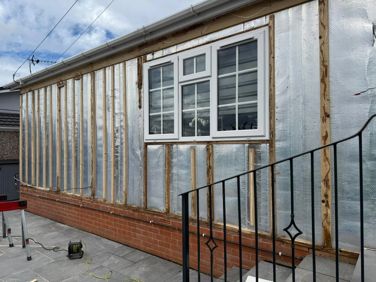 Park home exterior with insulation and window being installed, construction tools on the ground.