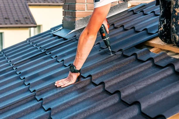 A person working on a blue metal roof, using a drill to secure the roof panels.