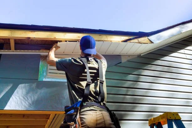 A person wearing a blue cap and work gear is installing or repairing a roof on a house.