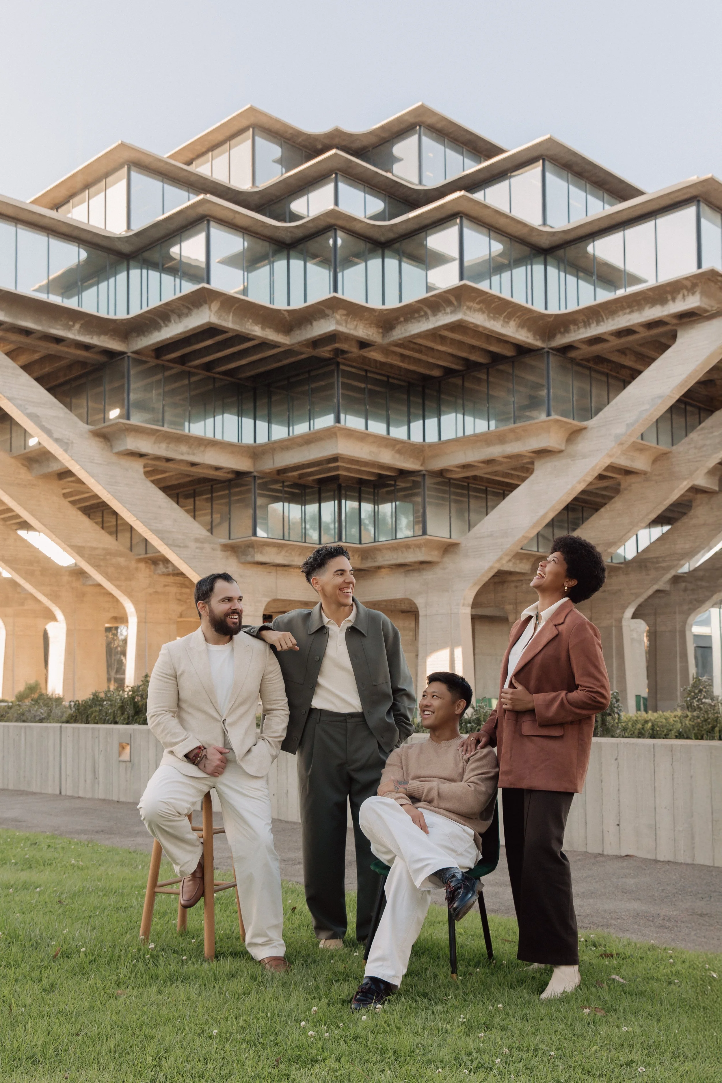 Four diverse people outdoors in front of a modern, multi-story building, engaging in conversation and sharing a laugh.