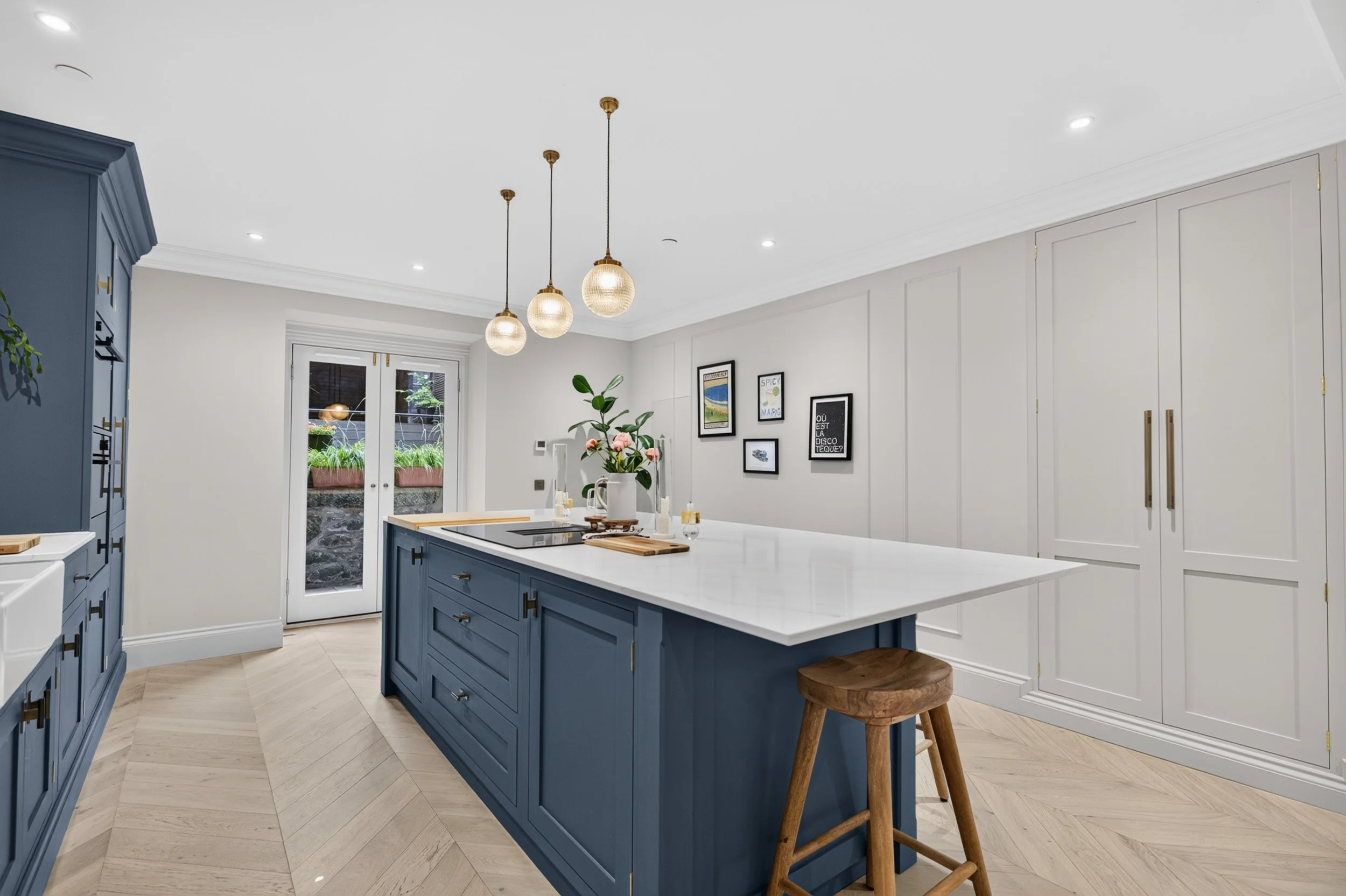 Modern kitchen with blue island, white countertop, and hanging pendant lights, decorated with artwork and plants.