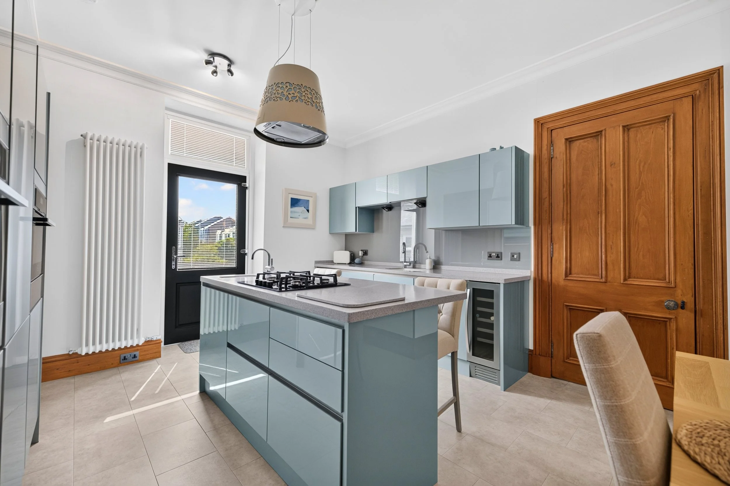 Modern kitchen interior with light blue cabinets, a kitchen island, a black door with a window, and wooden accents.