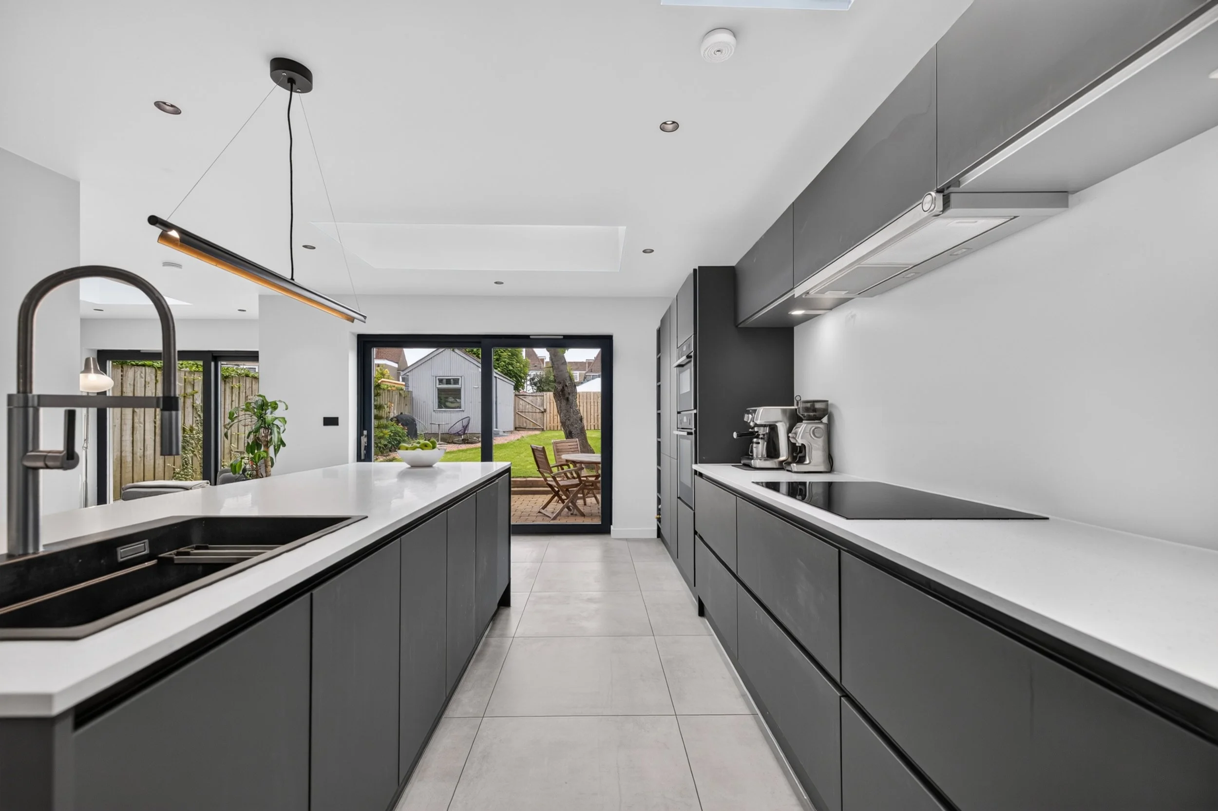 Modern kitchen with gray cabinets, white countertops, and a view into the backyard through sliding glass doors.