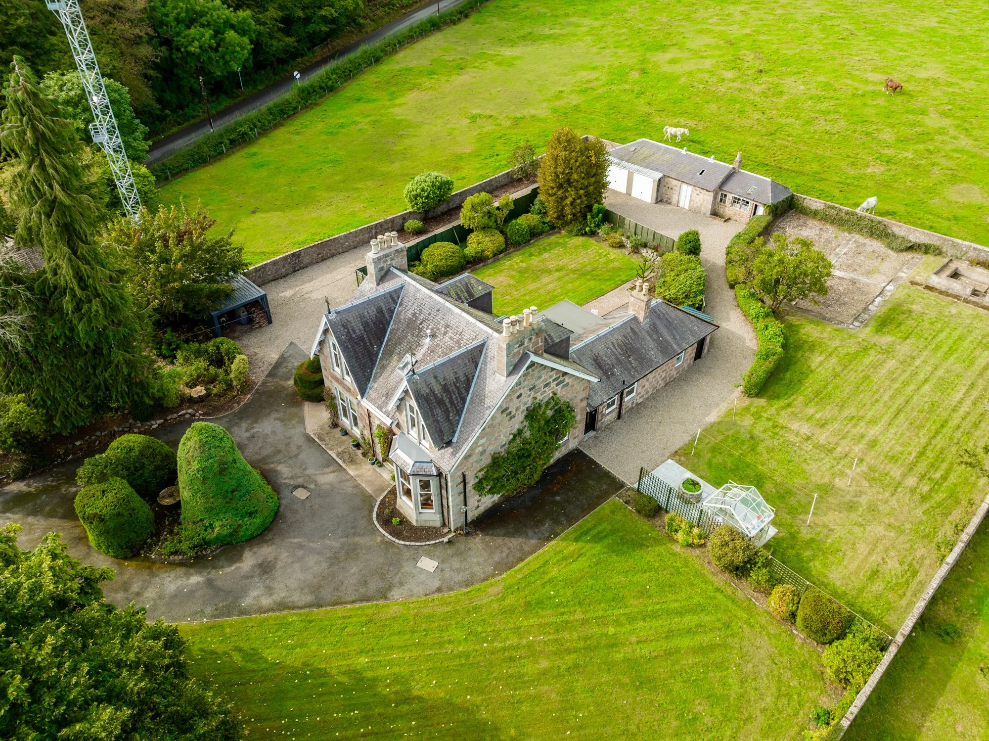 An aerial view of a house with a large garden and several horses grazing in a field nearby.