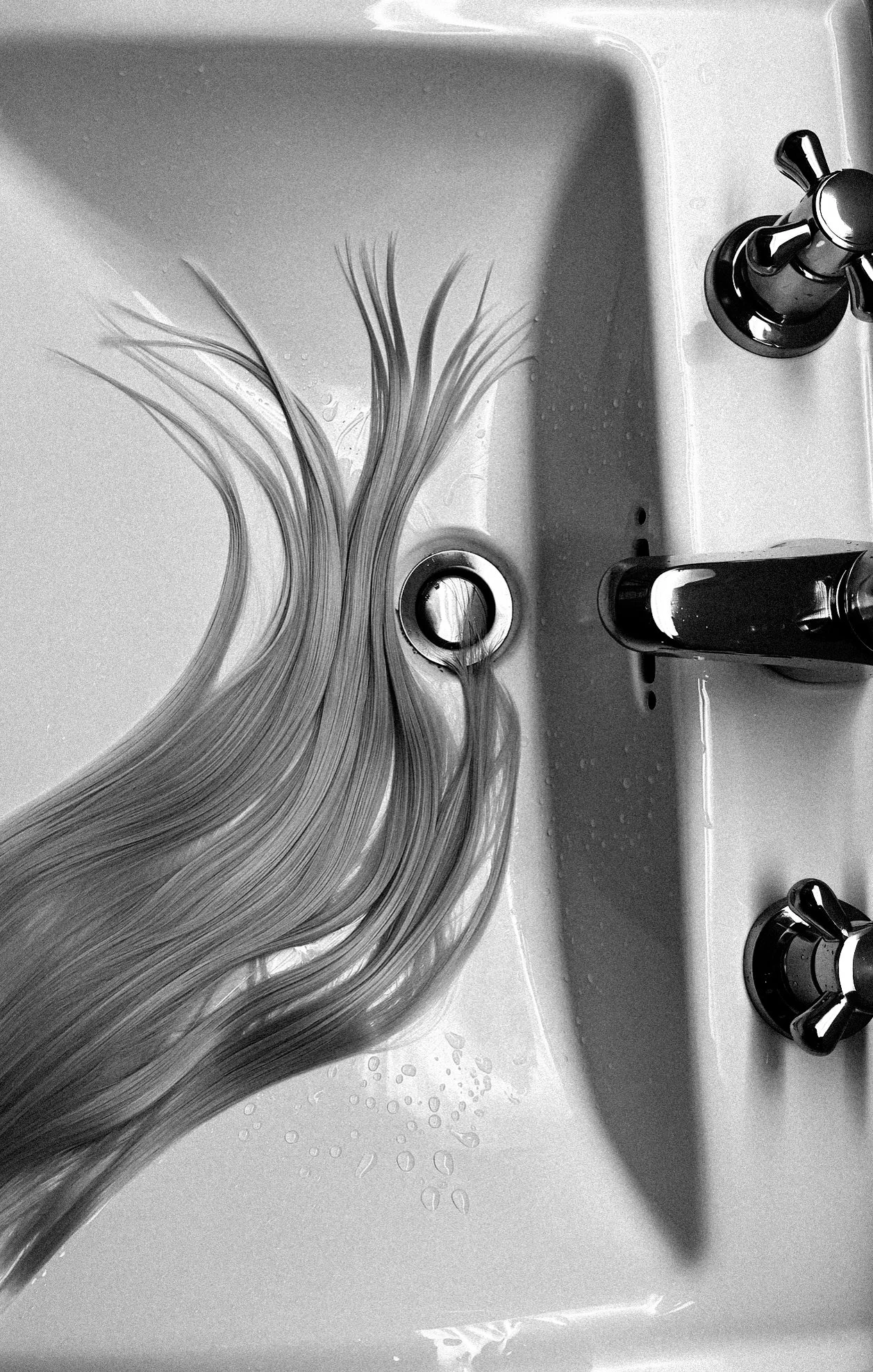 Long blonde hair in a sink with water flowing from the faucet.