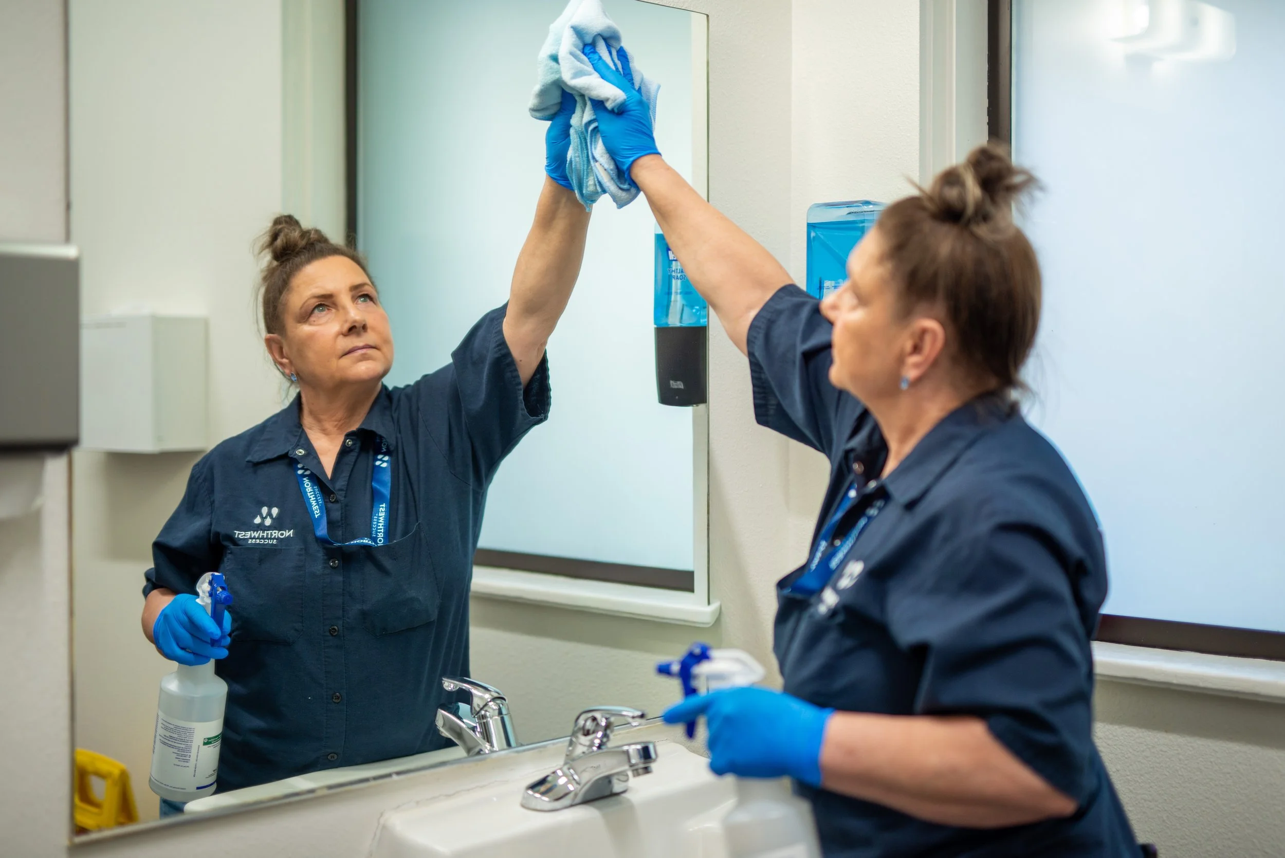 Northwest Success janitor cleaning bathroom mirror