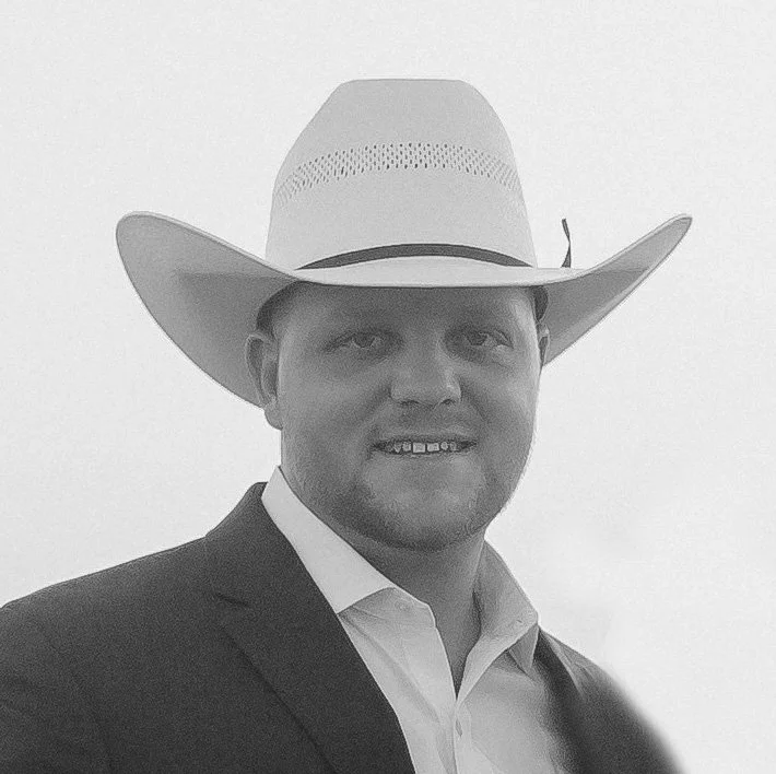 A man wearing a cowboy hat, a suit jacket, and a collared shirt, smiling at the camera.