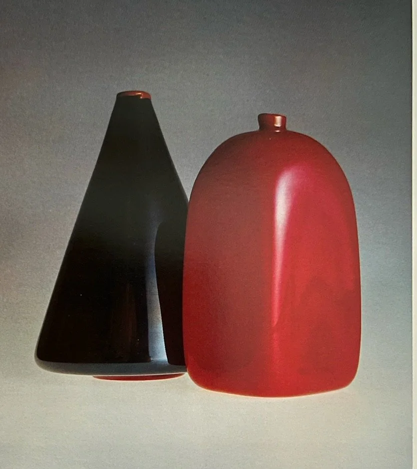 Two modern ceramic vases, one black and one red, with minimalist designs, displayed against a plain background.