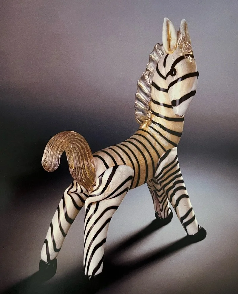 Decorative zebra figurine with black and white stripes, a golden mane and tail, standing on a dark surface against a plain background.