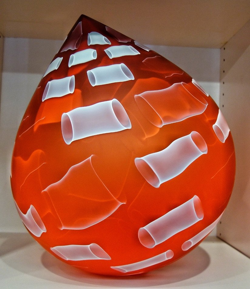 A decorative lamp shaped like a teardrop with a red base color and white, cylindrical glass tube patterns.