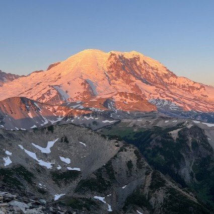 Mount Rainier in Washington State. A volcano with glaciated peaks during sunrise or sunset, with a clear blue sky. Photo taken by Luc Gensler