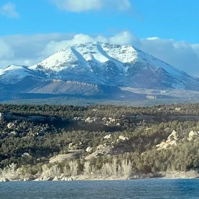 Snow-capped mountain in Utah with forests and water in the foreground. Photo taken by Luc Gensler.
