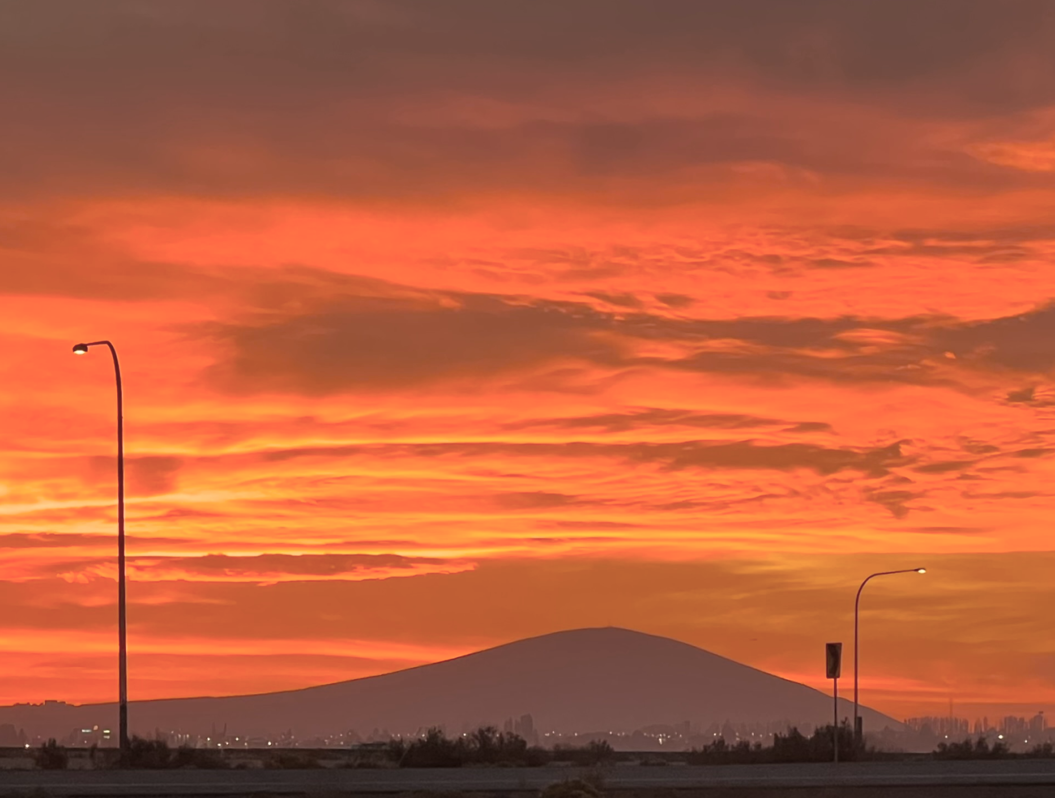 A sunset over Rattlesnake Mountain with orange, pink, and purple clouds, streetlights along a road in the foreground.