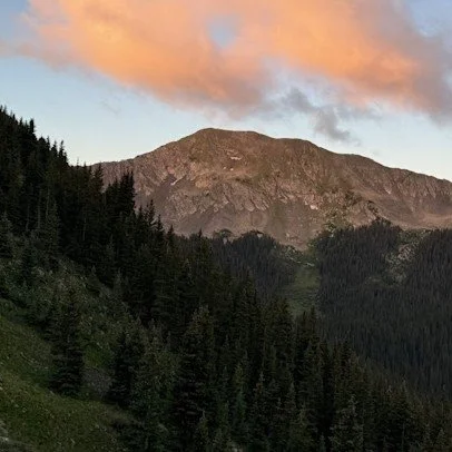 Photo of a mountain range with a partly cloudy sky at sunrise or sunset on Wheeler Peak, the highest point in New Mexico. Photo was taken by Luc Gensler.