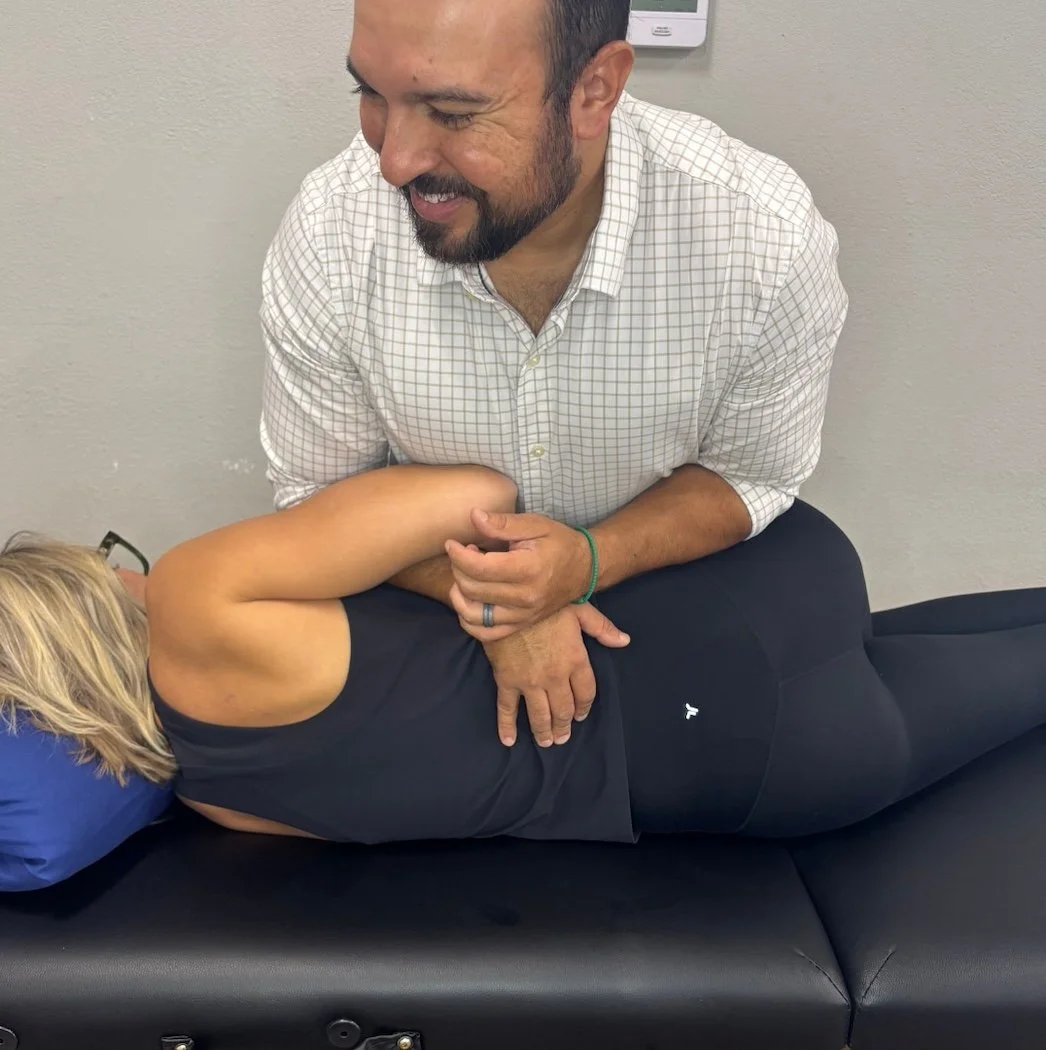 A chiropractor adjusting a woman lying face down on an examination table in a medical office.
