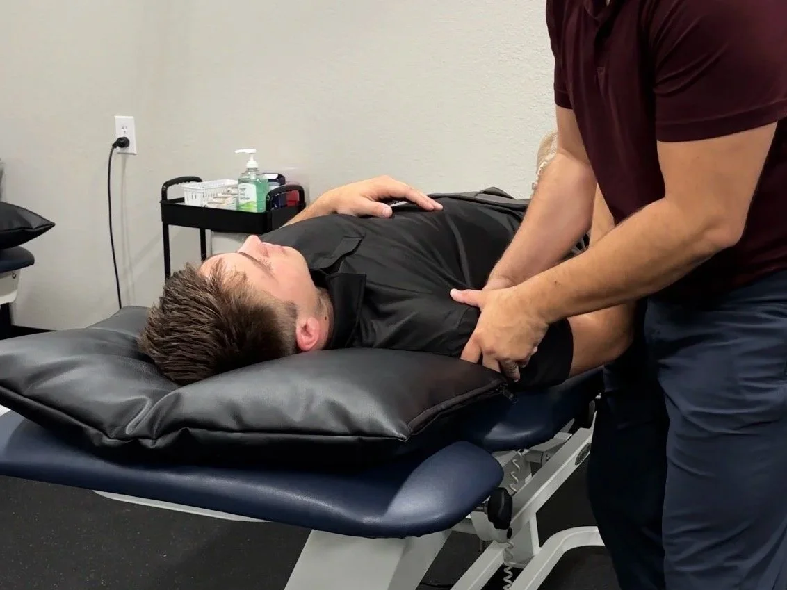 Person lying on a medical examination table receiving physical therapy or chiropractic treatment from a healthcare professional.