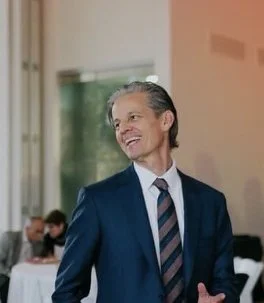 A smiling man in a blue suit and striped tie at a formal event