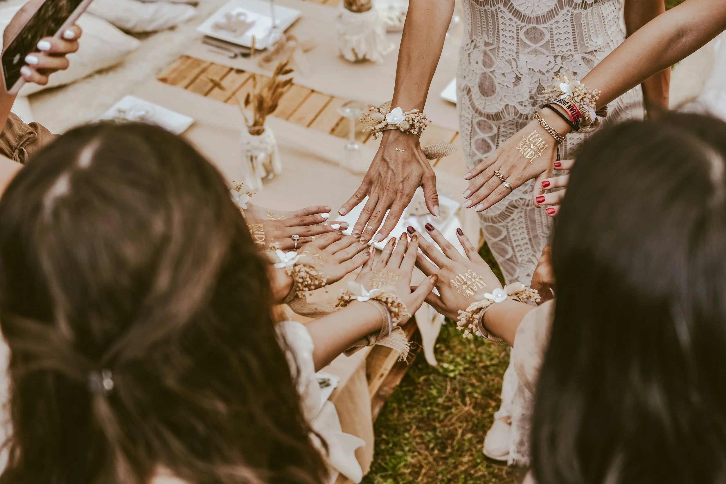 Group of women with different skin tones displaying painted hands with 'Team Bride' and 'Bride' written, during a wedding celebration outdoor.